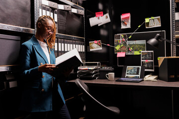 African american woman police investigator reading case file in office room. Private detective...
