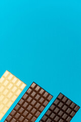 Three bars of dark, milk and white chocolate on a blue background. High quality photo