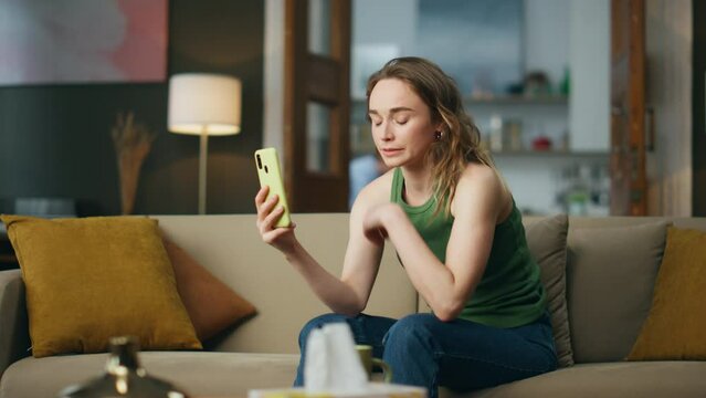 Unhappy woman looking telephone screen at living room. Sad girl getting bad news