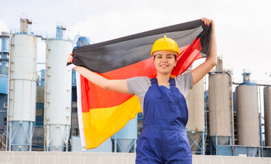 Cheerful female worker in hardhat with german flag standing in front of factory