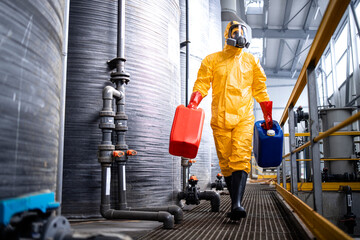 Factory worker in protective equipment walking by acid storage tanks and carrying aggressive and...
