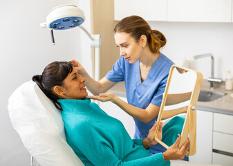 Woman beautician examining face skin of female patient before cosmetology procedure in beauty clinic