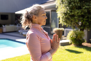 Happy senior caucasian woman doing yoga, meditating in sunny garden