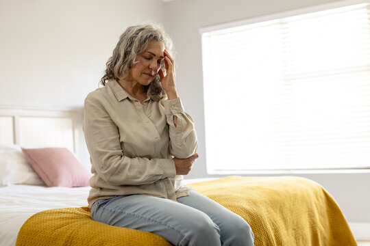 Worried senior caucasian woman sitting on bed holding her head