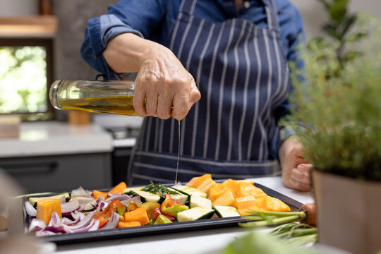 Midsection of senior caucasian woman pouring olive oil on vegetables in kitchen