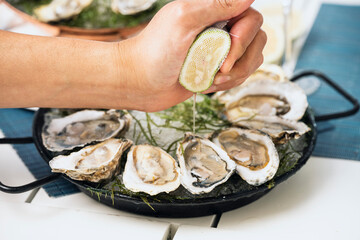 ostras frescas al natural en plato negro con limón exprimido por una mano en fondo blanco