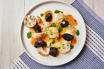pescado cocinado con salsa naranja y vegetales en plato blanco sobre mantel azul