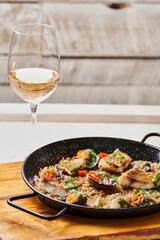 mariscos cocinados con vegetales y arroz sobre plato negro en una tabla de madera con una copa de vino