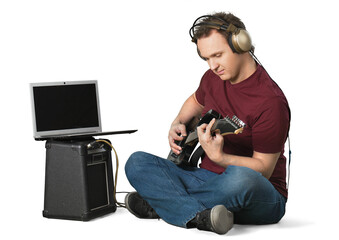 Portrait of handsome young man in headset sitting and playing guitar near laptop and speaker