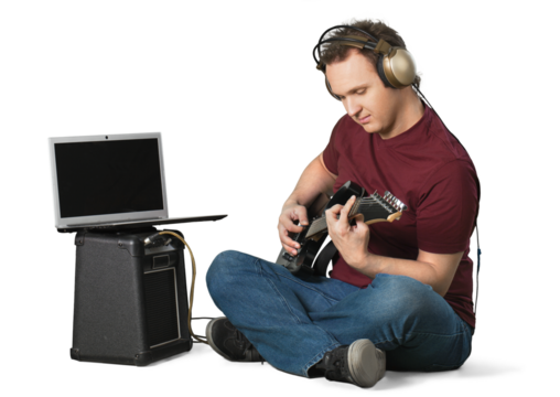 Portrait of handsome young man in headset sitting and playing guitar near laptop and speaker