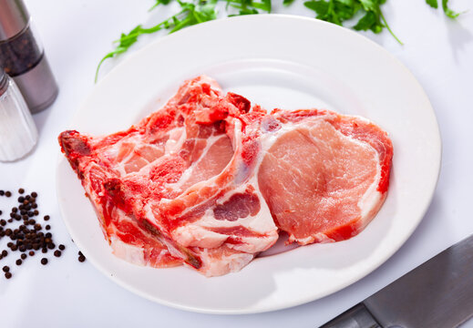 Fresh raw pork loin chops on plate on white background with condiments
