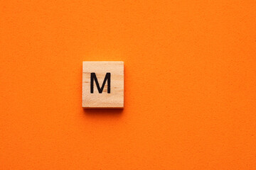Alphabet capital letter M on wooden square tile - Orange foamy background