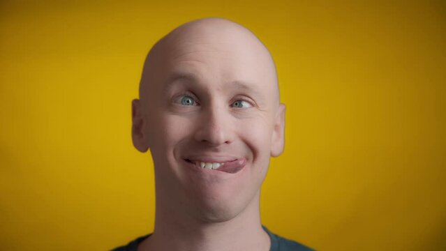 Man makes a goofy face with his tongue sticking out to the side and his eyes crossed on a yellow background, Real time.