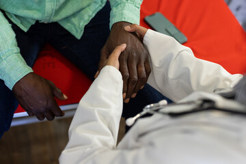 Midsection of biracial female doctor examinating hand of african american male patient