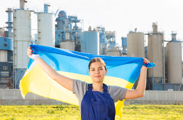Against the backdrop of a factory located outside the city, a balanced girl in a worker overalls...
