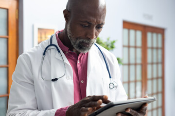 African american male doctor wearing stethoscope using tablet at doctor's office
