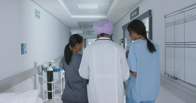 Diverse doctors and nurse talking and walking through corridor at hospital, in slow motion