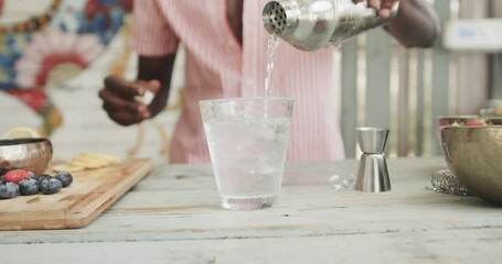 Midsection of african american barman pouring cocktail behind the counter at beach bar, slow motion