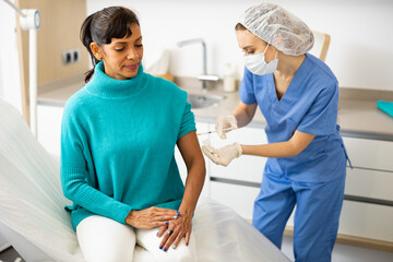 Portrait of young adult woman getting injection during visit at doctors office