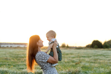 a young woman and her little daughter in a field at sunset in the backlight. Mother and 2 year old daughter face to face. Country life. Happy childhood in unity with nature. Summer rest.