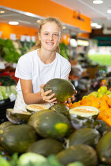 Fototapeta premium Young positive girl choosing sweet fresh melon at grocery section of supermarket