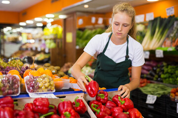 Young blonde salesgirl at her first job, selling bell pepper in vegetable shop