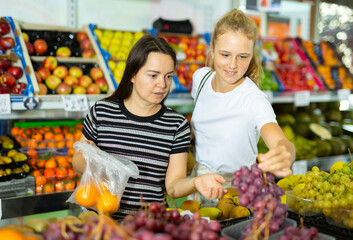 Two positive woman choosing sweet fresh grape at grocery section of supermarket