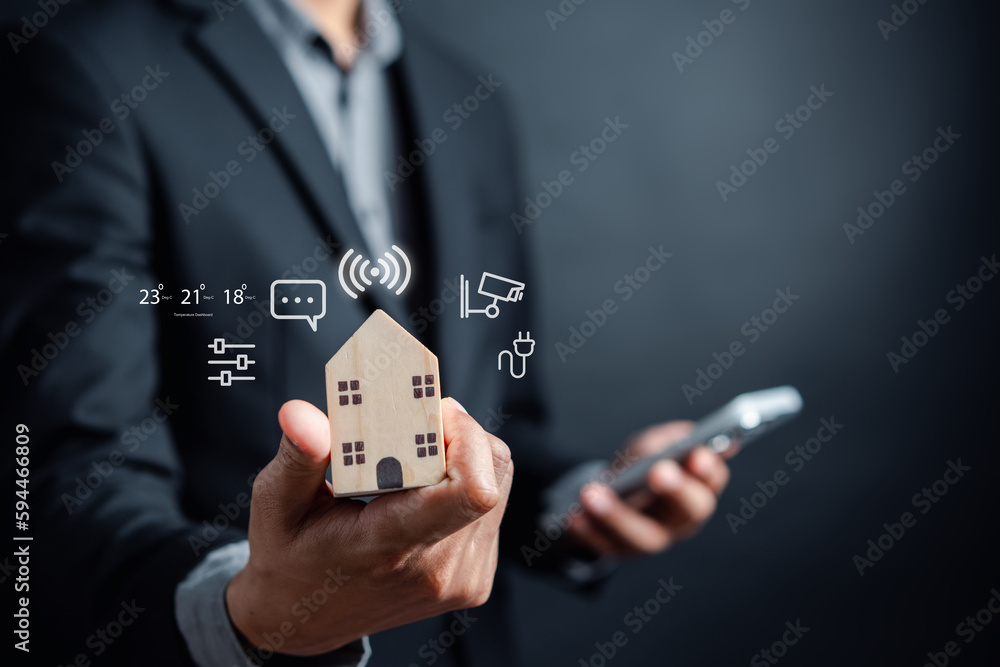 Poster Smart home digital remote control on smartphone concept. internet of things in technology control. Businessman holding wooden house with virtual smart home icon function.