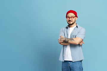 Portrait of handsome smiling asian  man with arms crossed and stylish tattoo isolated on blue...