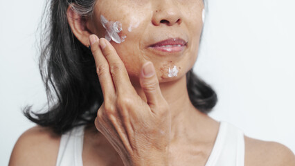 Close up face of female elderly mature older asian chinese housewife applies anti aging facial cream on face, old skincare treatment