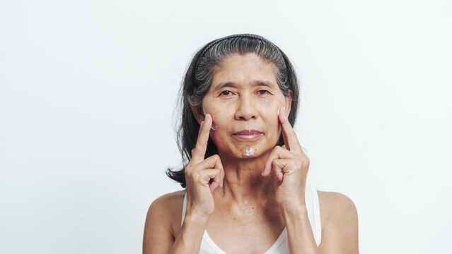 Close up face of female elderly mature older asian chinese housewife applies anti aging facial cream on face, old skincare treatment