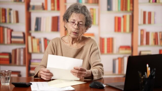 Angry stressed elderly old woman 80s, opening envelope reading bad news and tears up mail letter. Mad female feels frustrated by high bills, bank debt, tax invoice or mistake.