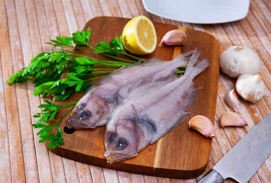 Uncooked roosterfish with greens and garlic on wooden board before cooking