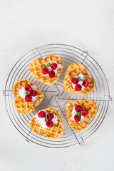 Viennese heart-shaped waffles with cream and raspberries. On a serving metal stand. White background. Top view
