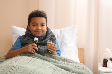 African-American boy taking cough syrup on bed at home, space for text. Cold medicine