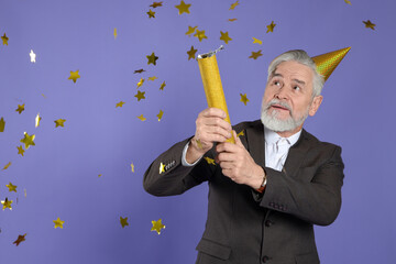 Man blowing up party popper on purple background