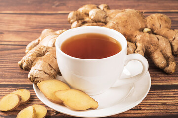 Cup of hot ginger tea with ginger root and slices on wood table.