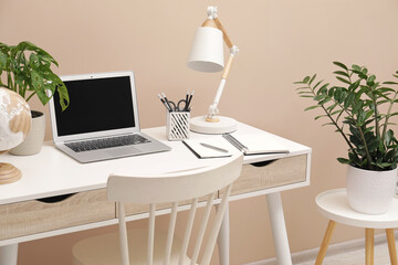 Cozy workplace with modern laptop on desk and comfortable chair at home