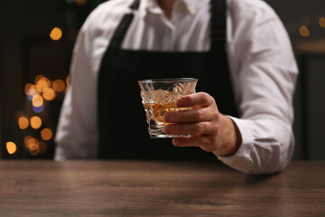 Bartender with glass of whiskey at bar counter indoors, closeup