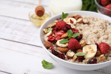 Delicious oatmeal with freeze dried berries, banana, nuts and mint on white wooden table, closeup. Space for text