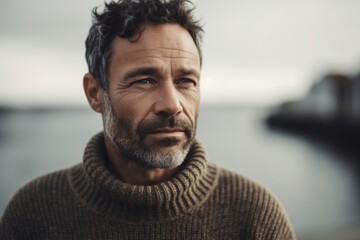 Obraz na płótnie Canvas Environmental portrait photography of a tender man in his 40s wearing a cozy sweater against a water or ocean background. Generative AI