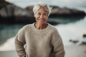 Fototapeta na wymiar Portrait of a smiling senior woman standing on the beach at sunrise