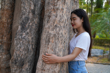 A woman in a white T-shirt embraces a large tree.  With a love of nature, protect the trees.