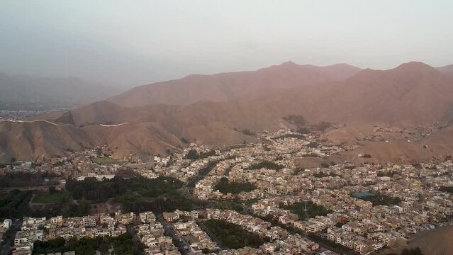 Panoramic of a town next to mountains during sunset in the Las Vi&ntilde;as neighborhood of La Molina, Lima, on the Peruvian coast. Smooth upward movement with drone.