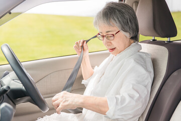 自動車の運転席に乗りシートベルトを締めるアジア人の高齢者ドライバー

