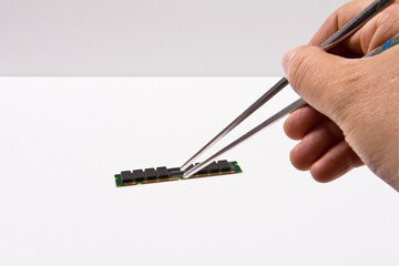 A hand is holding a piece of computer chip with a pair of tweezers.