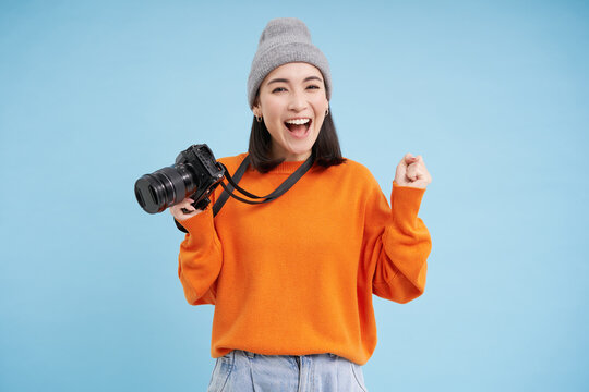 Stylish asian girl with digital camera, taking pictures. Woman photographer smiling, standing over blue background