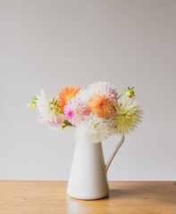 Vertical close up of colourful dahlia flowers in white jug on oak table against neutral wall background with vintage filter effect