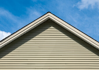 Top of House. Triangle House Top in the blue sky background. Gray vinyl wooden siding panel on the house. - obrazy, fototapety, plakaty