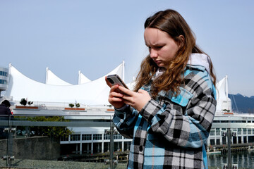 teenage tourist girl walks while it is necessary Play with Vancouver in city center at Waterfront station girl against background of white sails looks at phone busy looking for route geolocation